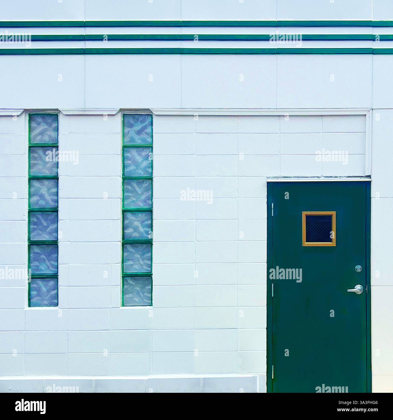Une porte verte minimaliste avec une petite fenêtre sertie contre une façade géométrique blanche avec des fenêtres verticales en blocs de verre et des lignes Art déco. Banque D'Images