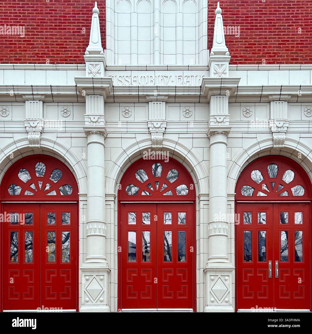 Entrée de hall d'assemblage néoclassique avec portes rouges éclatantes, détails complexes en pierre blanche et grandes fenêtres cintrées à Chicago - Image de stock capturée avec un smartphone