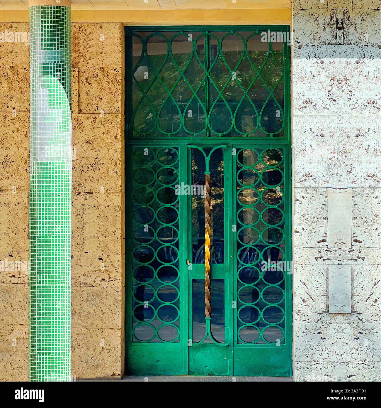 Porte en métal vert des années 1930 avec des motifs géométriques complexes et une poignée en laiton torsadée, complétée par une colonne en mosaïque à Varsovie, en Pologne Banque D'Images