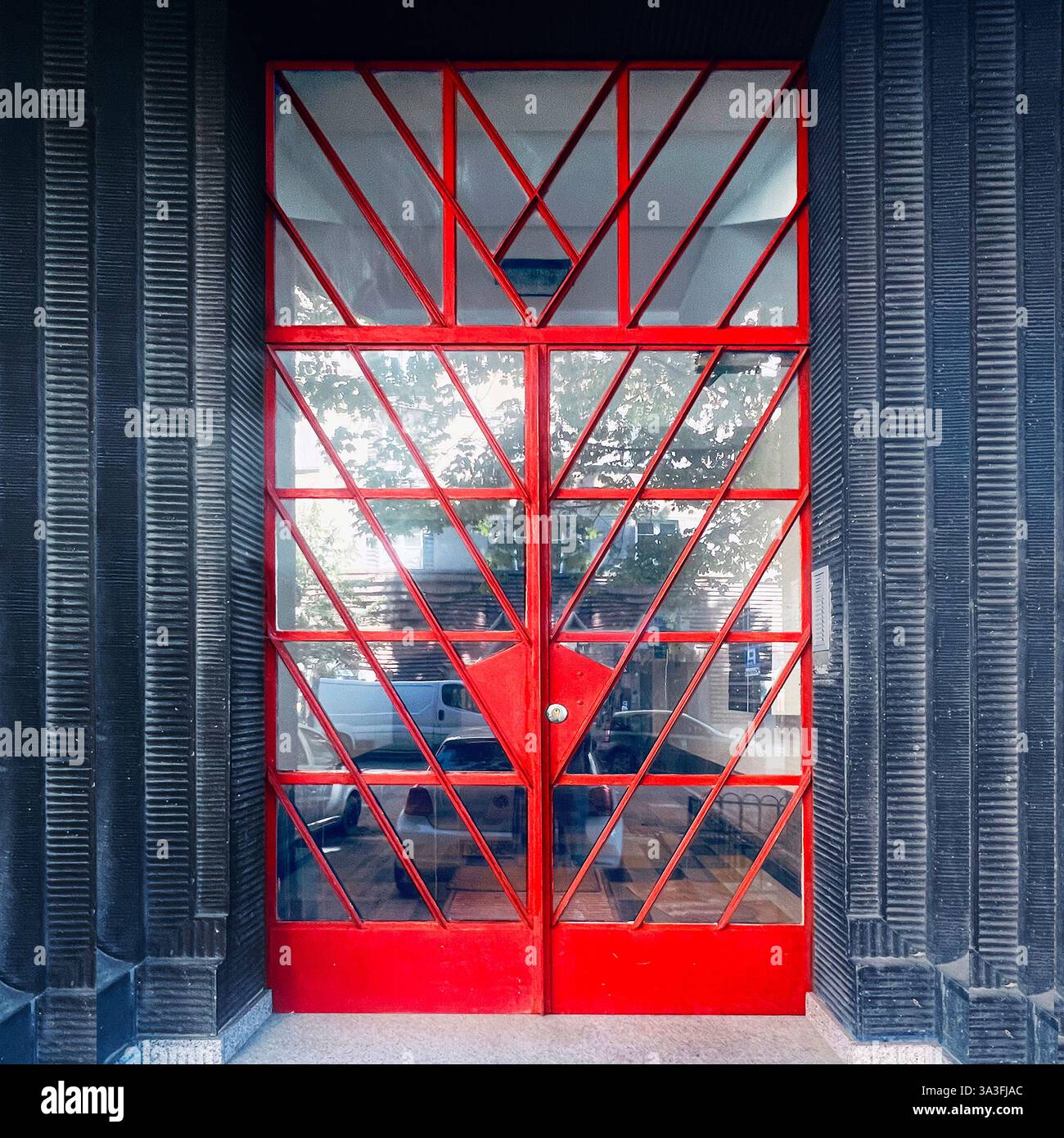 Entrée moderniste à Cracovie, en Pologne, avec des portes en fer à panneaux de verre géométriques rouges dans une façade noire texturée, modernisme du XXe siècle Banque D'Images