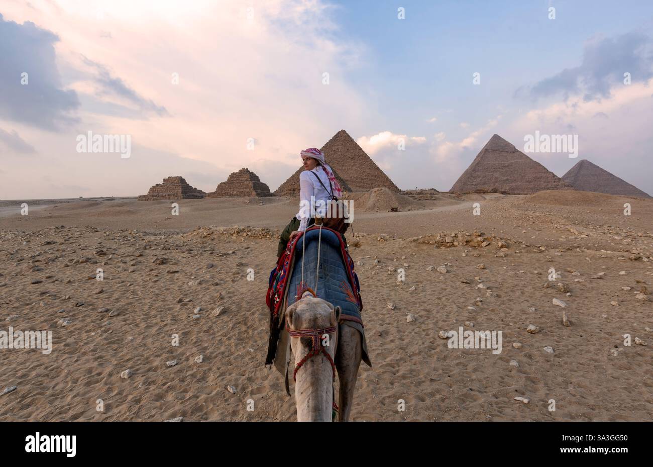 Chameaux dans Gizeh Pyramid Complex - Une femme dans un turban rouge chevauchant un chameau à travers les minces dunes de sable - le Caire, Egypte Banque D'Images