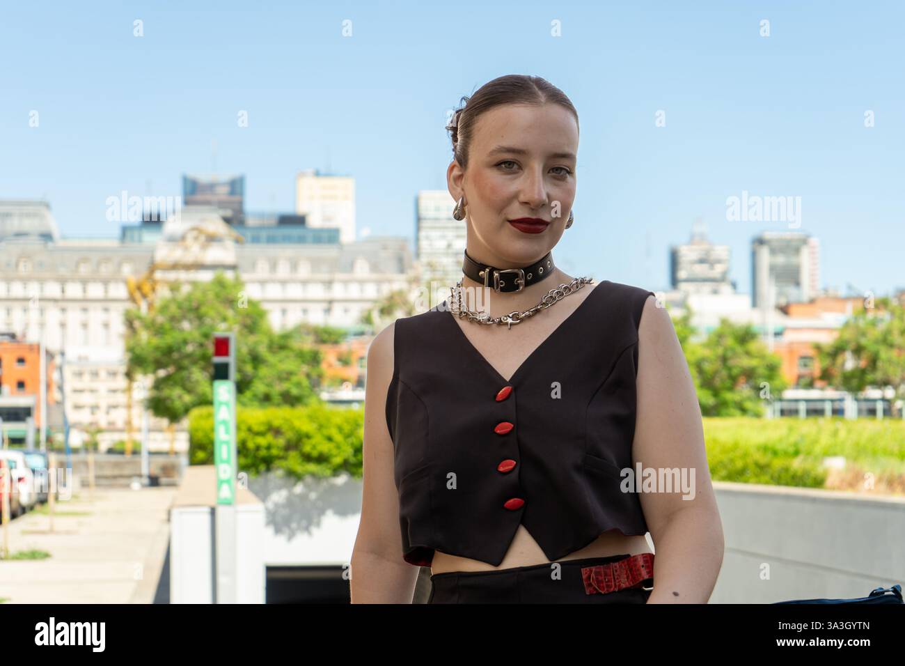 Jeune femme à la mode se tient dans un environnement urbain moderne, mettant en valeur son style unique dans un contexte de bâtiments contemporains Banque D'Images