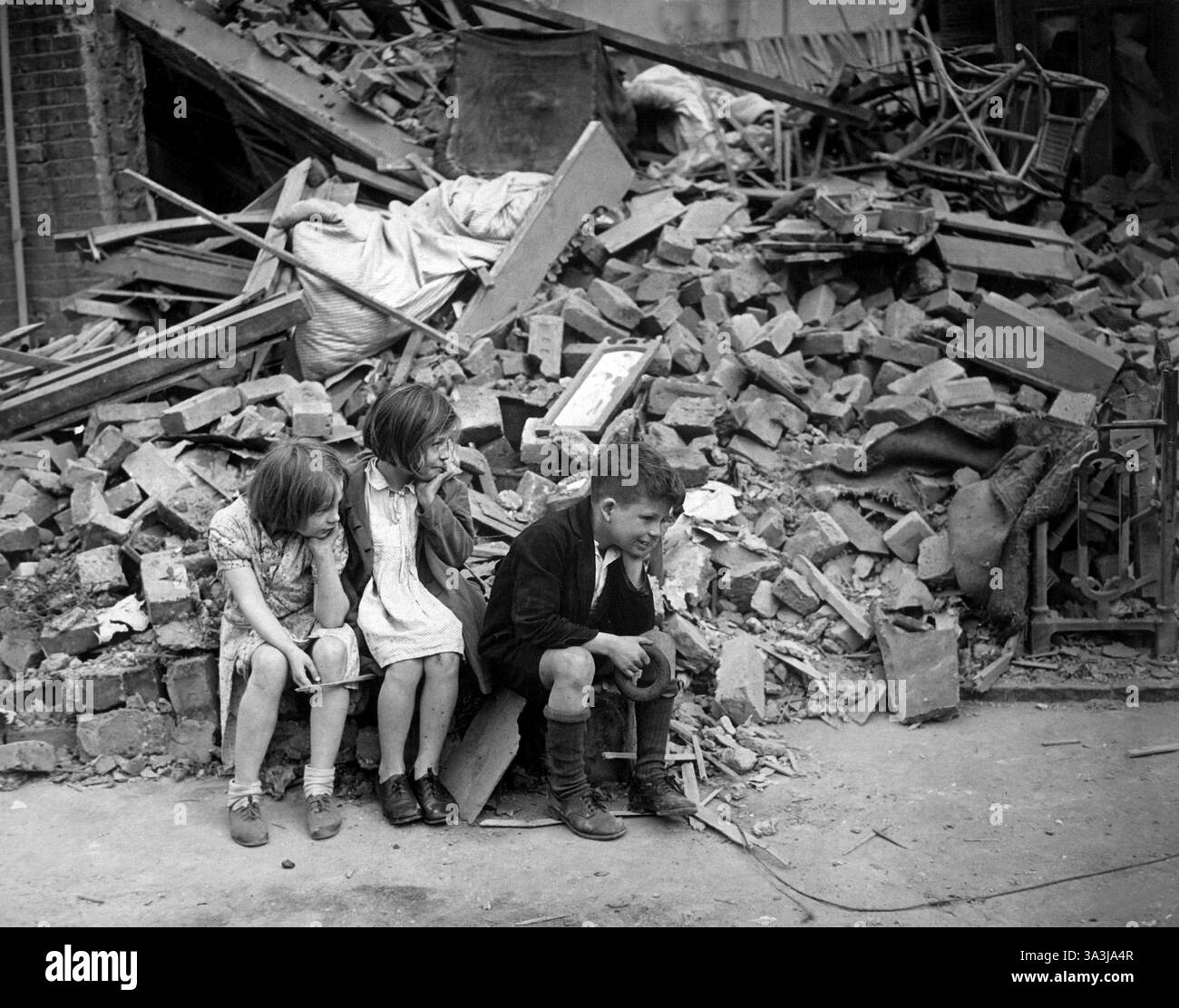 Le Blitz de la seconde Guerre mondiale est une campagne allemande de bombardement contre le Royaume-Uni, pendant huit mois, du 7 septembre 1940 au 11 mai 1941, pendant la seconde Guerre mondiale. - Les enfants d'une banlieue est de Londres, qui ont été rendus sans abri par les bombes aléatoires des raids de nuit nazis, attendant à l'extérieur de l'épave de ce qui était leur maison. Septembre 1940. Banque D'Images