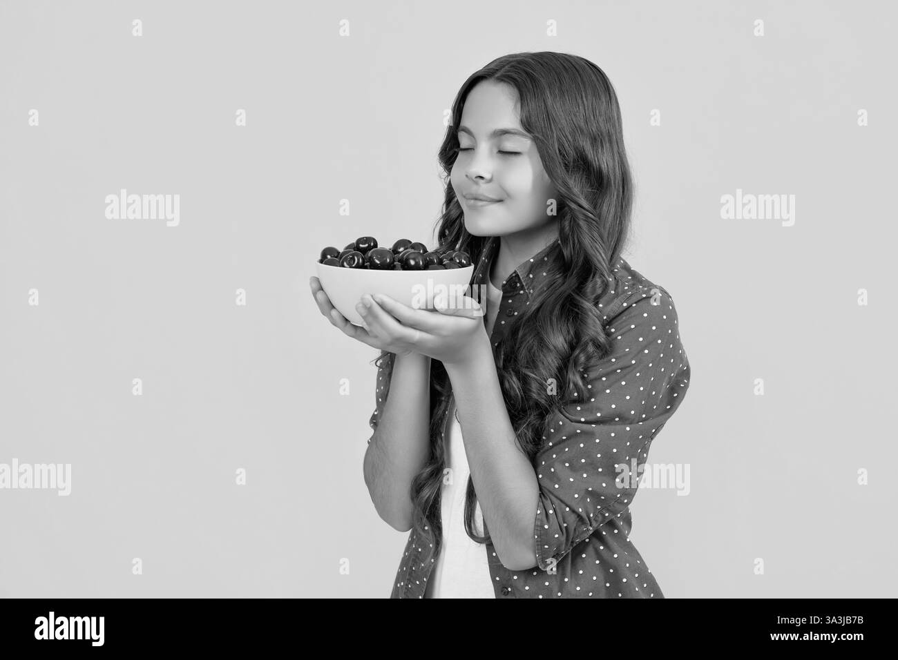 bonne jeune fille qui sent le bol de cerise sur fond jaune Banque D'Images