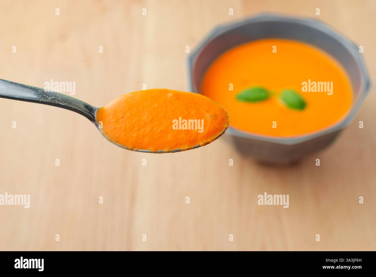 Une cuillerée de soupe est maintenue contre un bol de soupe. La cuillère est en argent et le bol est en céramique Banque D'Images