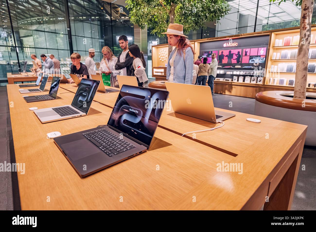 17 janvier 2025, Abu Dhabi, Émirats arabes Unis : jeune femme essayant un ordinateur portable dans un magasin d'électronique Apple moderne, avec d'autres clients naviguant sur des produits Banque D'Images