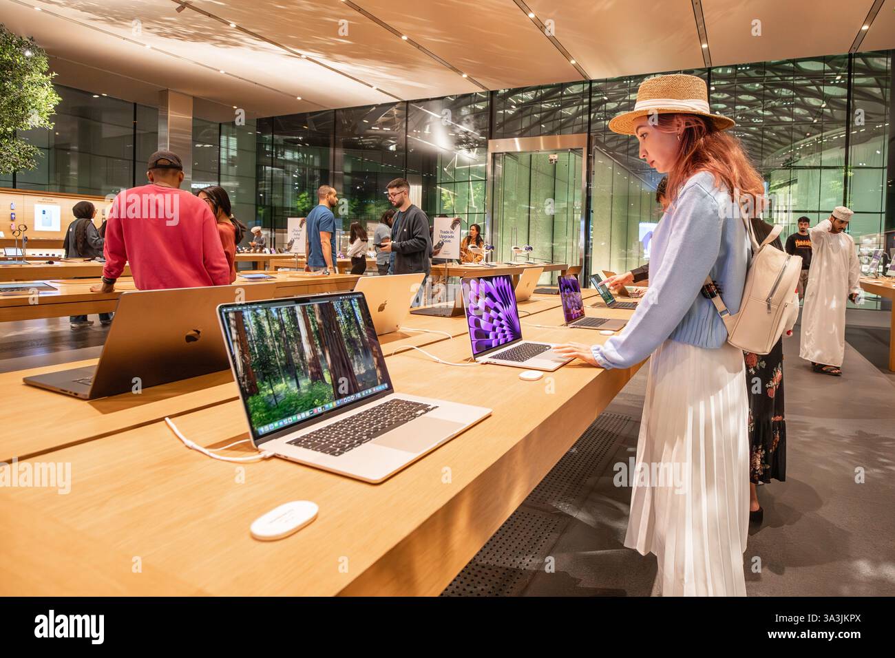 17 janvier 2025, Abu Dhabi, Émirats arabes Unis : jeune femme essayant un ordinateur portable dans un magasin d'électronique Apple moderne, avec d'autres clients naviguant sur des produits Banque D'Images