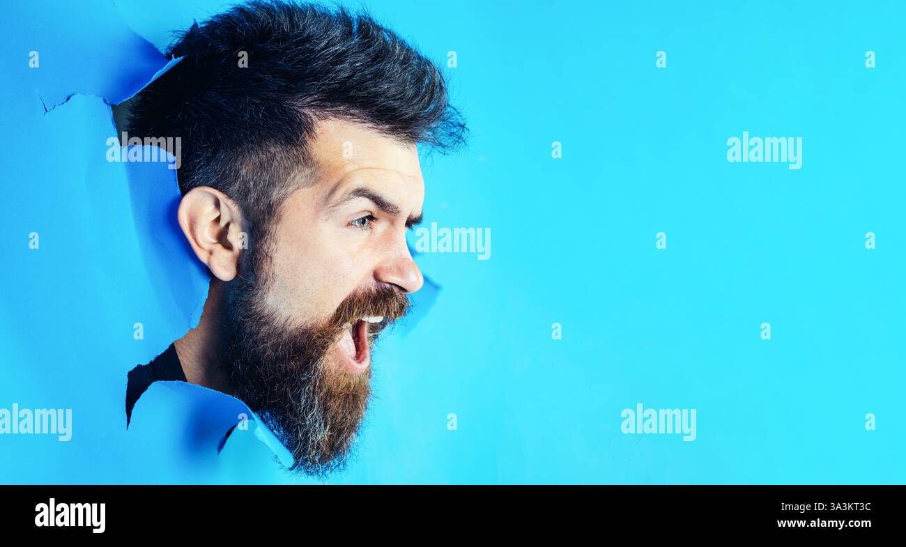 Bel homme barbu avec une coiffure élégante regardant à travers le trou dans le papier. Un homme heureux faisant un trou dans le mur de papier. Tête mâle regardant à travers le trou. Vente, Banque D'Images