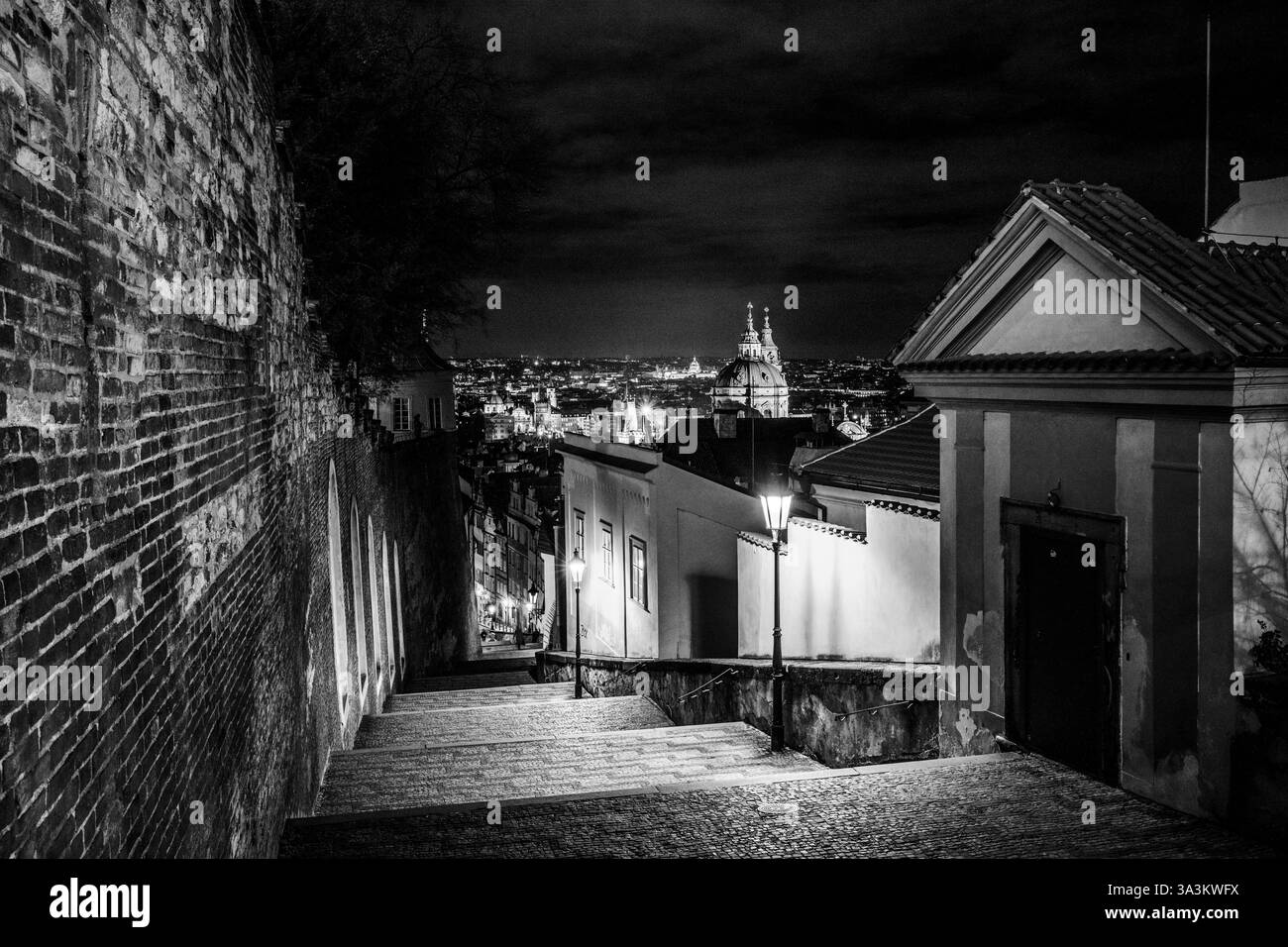 L'escalier menant au château de Prague brille doucement sous les lampadaires, offrant une vue tranquille sur la ville. L'architecture historique ajoute du charme à une promenade nocturne paisible. Banque D'Images