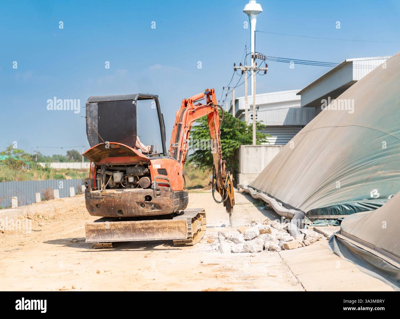 Excavatrice sur chenilles avec marteau de marteau hydraulique pour la destruction de la route en béton à l'usine. Banque D'Images