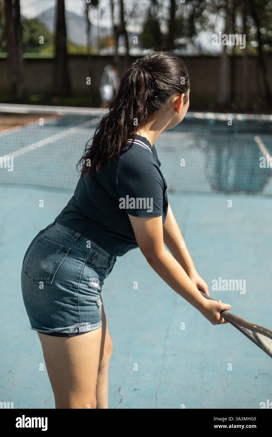 Une fille se tient dos à la caméra dans une position de service, se préparant à un service puissant pendant un match de tennis intense. Banque D'Images