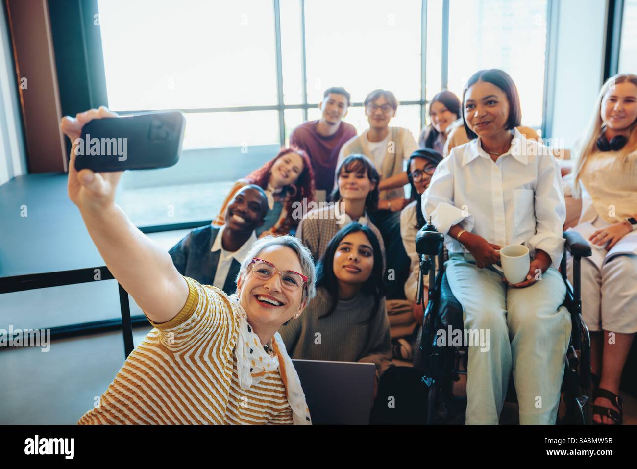Un enseignant joyeux capture un selfie avec un groupe diversifié d'élèves dans une salle de classe, mettant en évidence l'inclusivité, l'apprentissage et le travail d'équipe. Banque D'Images