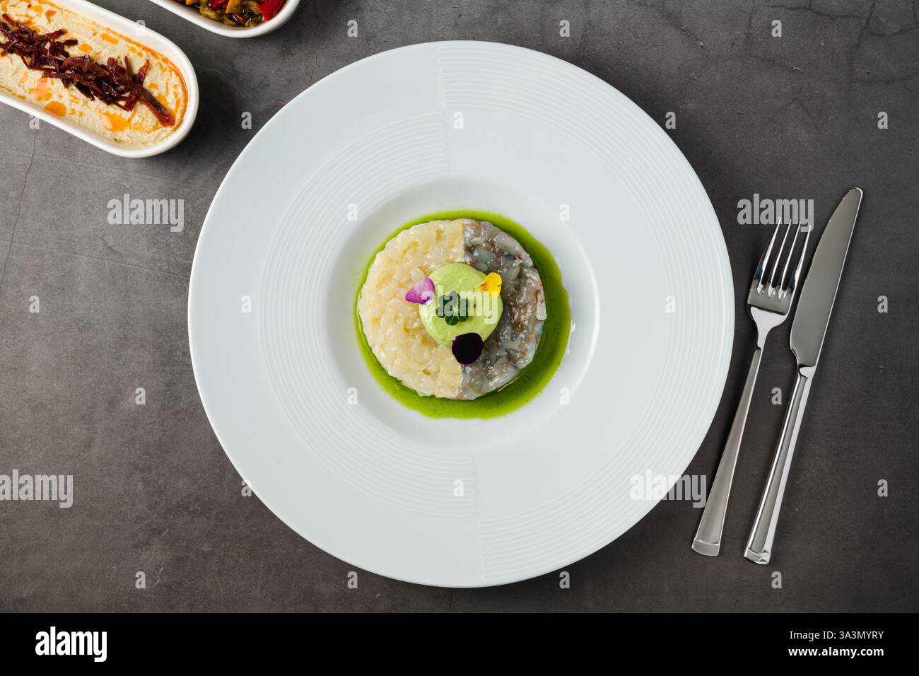 Tartare gourmand de crevettes et de poisson blanc avec mousse d'avocat, fleurs comestibles et sauce verte, servi dans une assiette blanche Banque D'Images