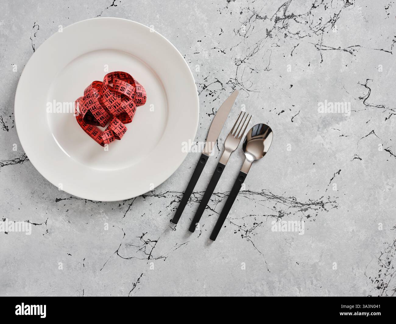 Ruban à mesurer sur une assiette blanche avec des couverts de côté symbolisant l'alimentation, la perte de poids et une nutrition saine Banque D'Images