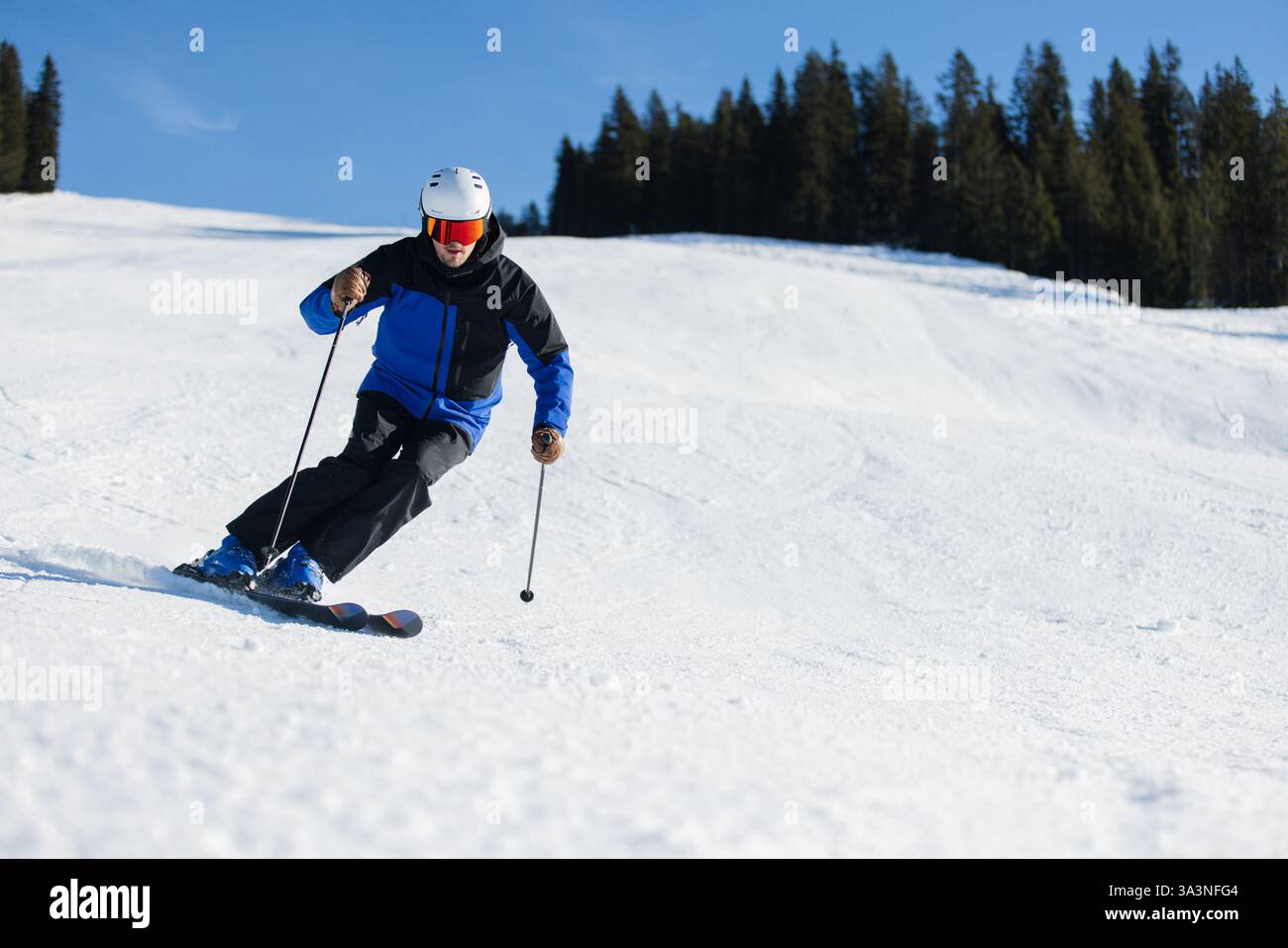 Skieur sculptant sur une pente enneigée à Kitzbühel sous un ciel bleu vif Banque D'Images