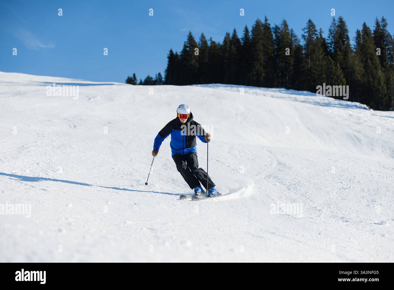 Skieur sculptant sur une pente enneigée à Kitzbühel sous un ciel bleu vif Banque D'Images