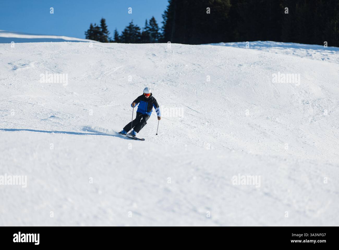 Skieur sculptant sur une pente enneigée à Kitzbühel sous un ciel bleu vif Banque D'Images