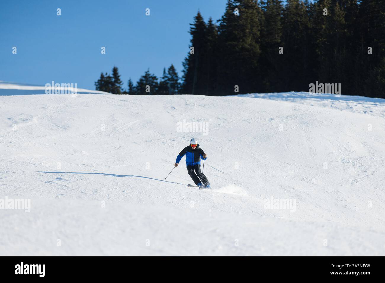 Skieur sculptant sur une pente enneigée à Kitzbühel sous un ciel bleu vif Banque D'Images