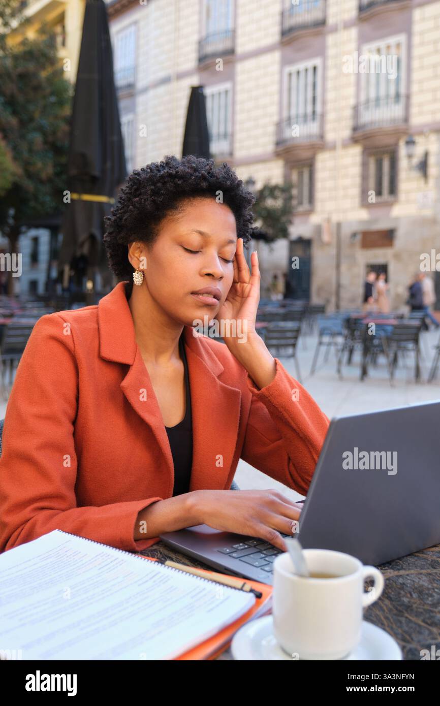 Femme stressée ayant mal à la tête tout en travaillant sur ordinateur portable au café en plein air Banque D'Images