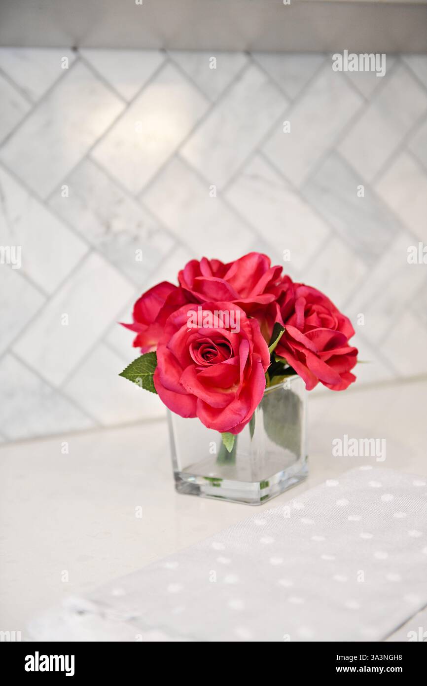 Roses rouges dans un vase en verre transparent sur un comptoir blanc avec une TIL Banque D'Images