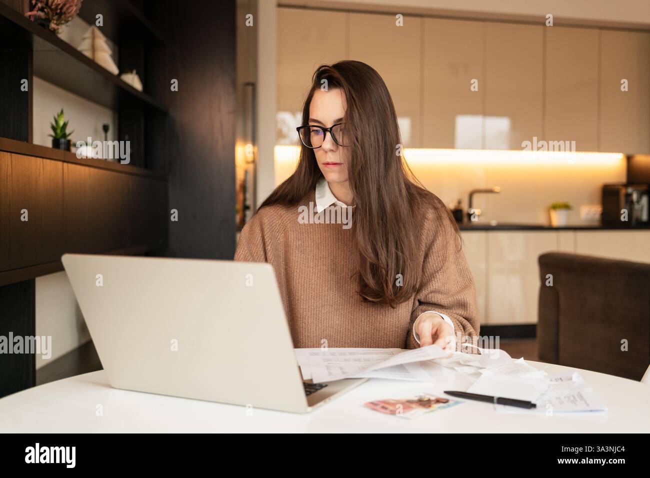 Femme avec de longs cheveux bruns payant des factures à la maison en utilisant l'ordinateur portable Banque D'Images