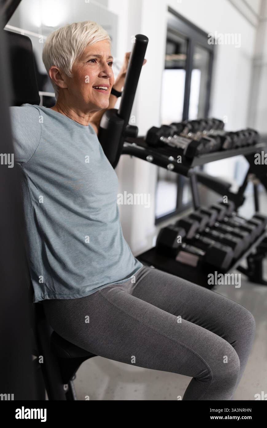 La participante fait de l'exercice au gymnase, en utilisant un équipement de musculation. Elle semble concentrée et déterminée pendant la routine d'exercice Banque D'Images
