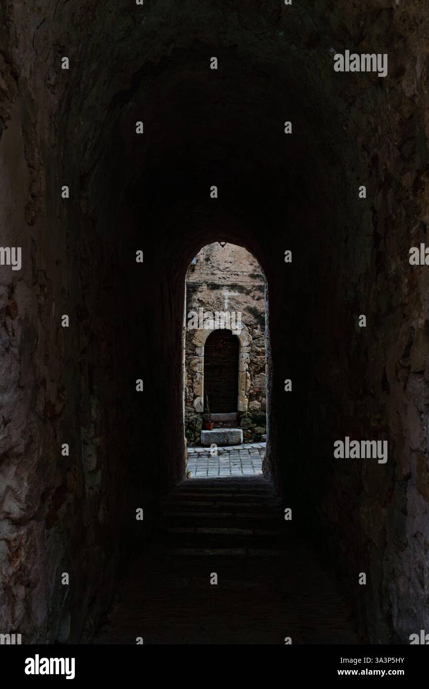 Une vieille porte en bois avec une arche en pierre se dresse au bout d'un passage sombre, avec des murs en pierre endommagés dans une ruelle du village historique. Un pot avec une plante Banque D'Images