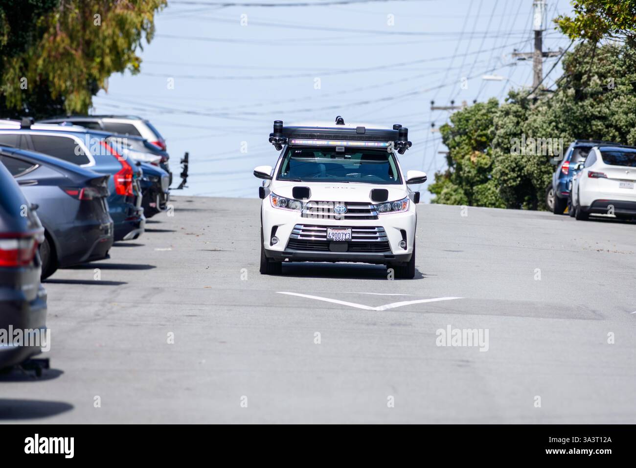 Amazon Zoox Toyota Highlander équipé de la technologie de conduite autonome navigue dans une rue en pente bordée de voitures garées dans un quartier résidentiel. Vue de face Banque D'Images
