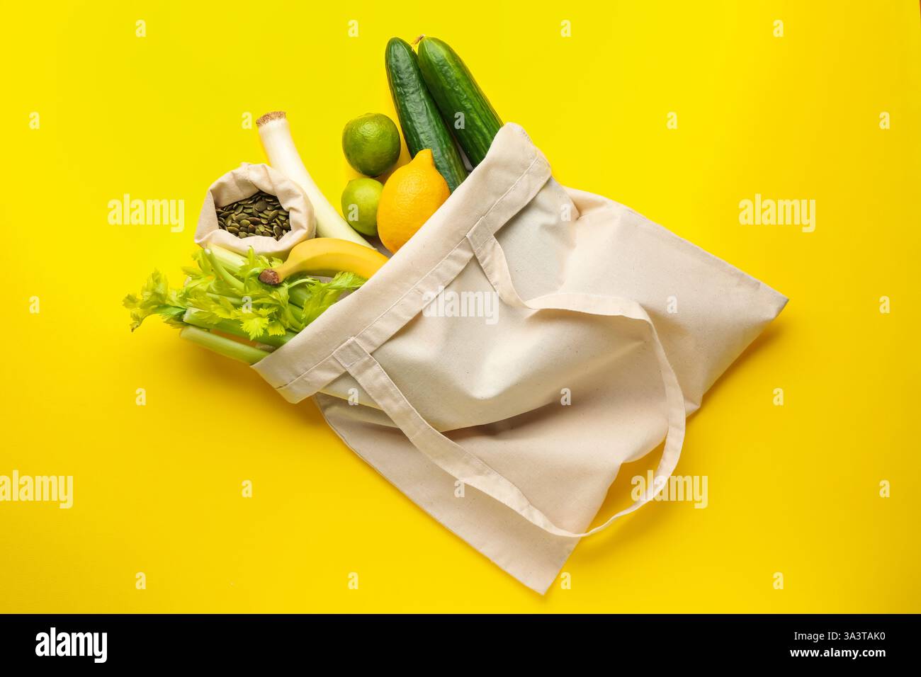 Sac écologique avec des légumes, des fruits et des graines de citrouille sur fond jaune, vue de dessus Banque D'Images