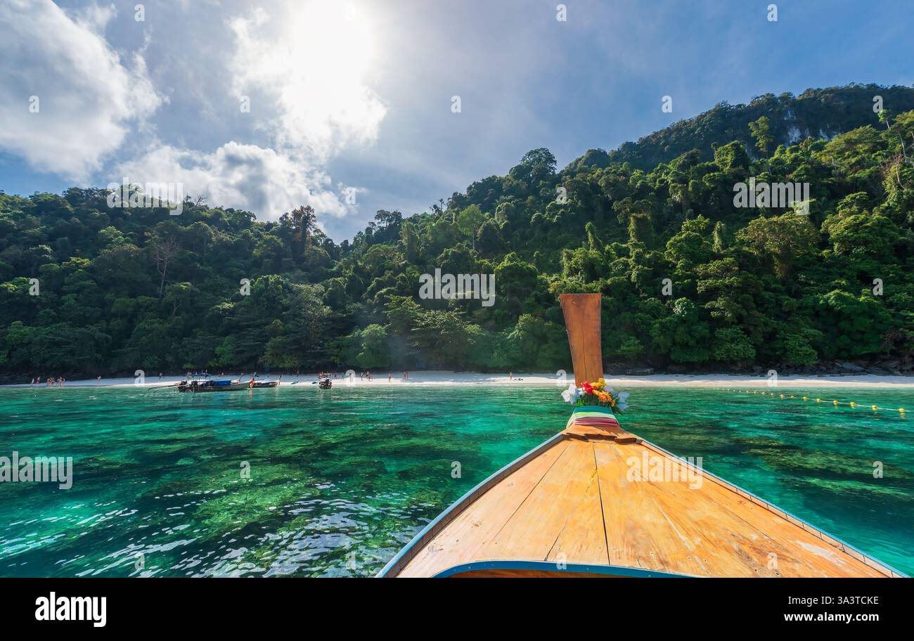 Monkey Beach, Thaïlande - une crique tropicale à couper le souffle avec des eaux turquoises, une jungle luxuriante et un bateau traditionnel à longue queue approchant du rivage Banque D'Images