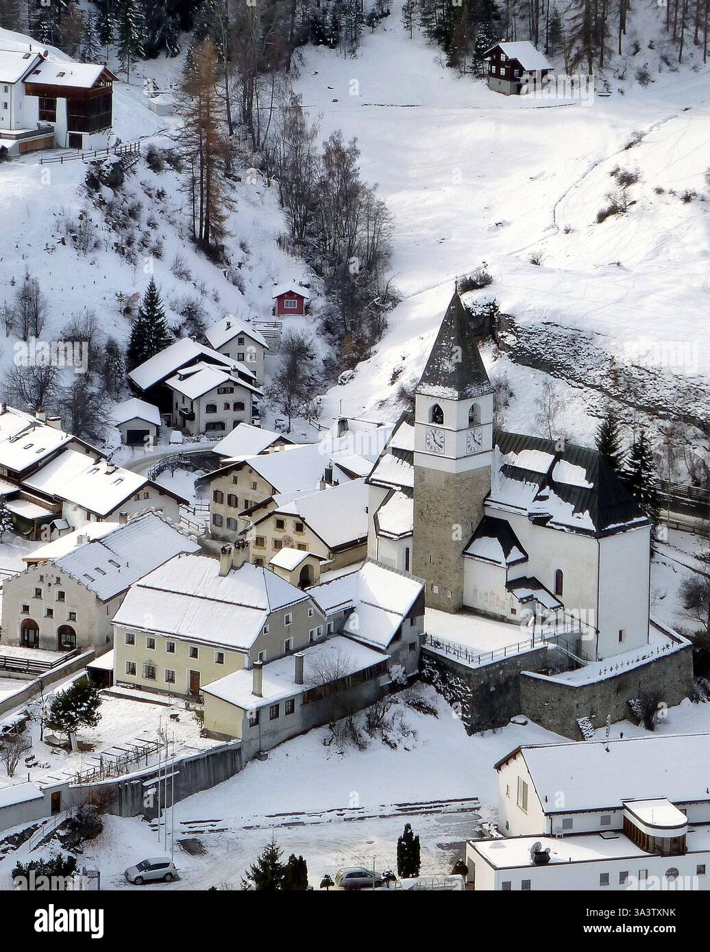 Image verticale du petit village alpin Tarasp avec des maisons enneigées et une église avec une tour de l'horloge en Suisse Banque D'Images