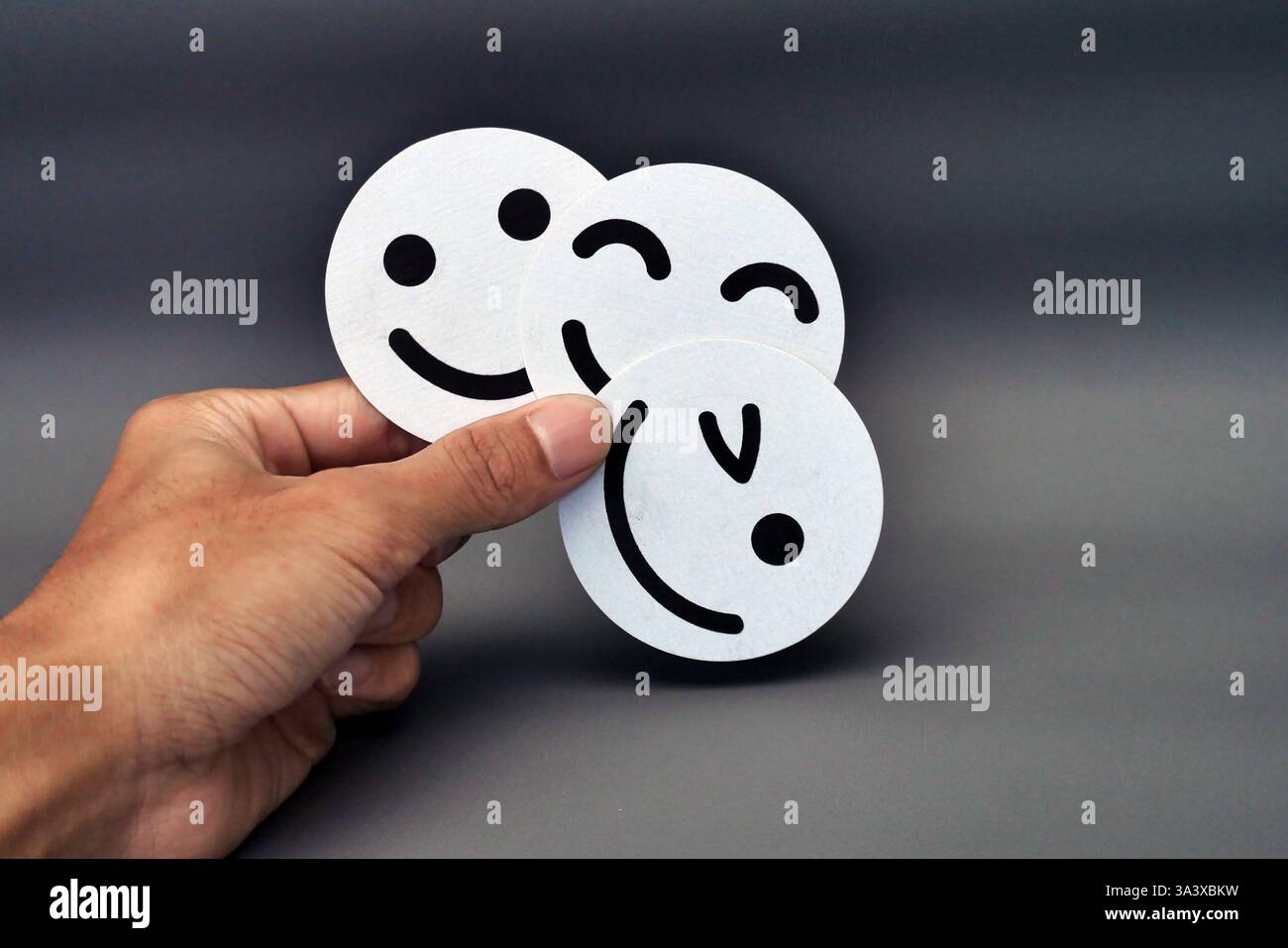 Main tenant trois Emojis White Smiley face sur fond sombre exprimant le bonheur, le plaisir et les émotions positives Banque D'Images