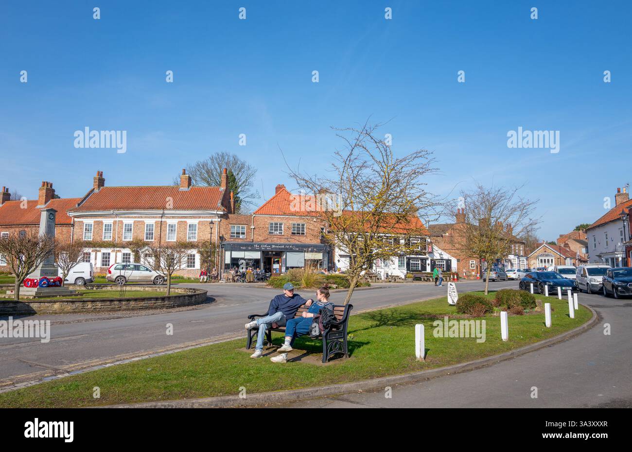 Couple parlant assis sur un banc en bois sur un bord d'herbe dans la place du marché dans le North Yorkshire ville de marché d'Easingwold. Banque D'Images