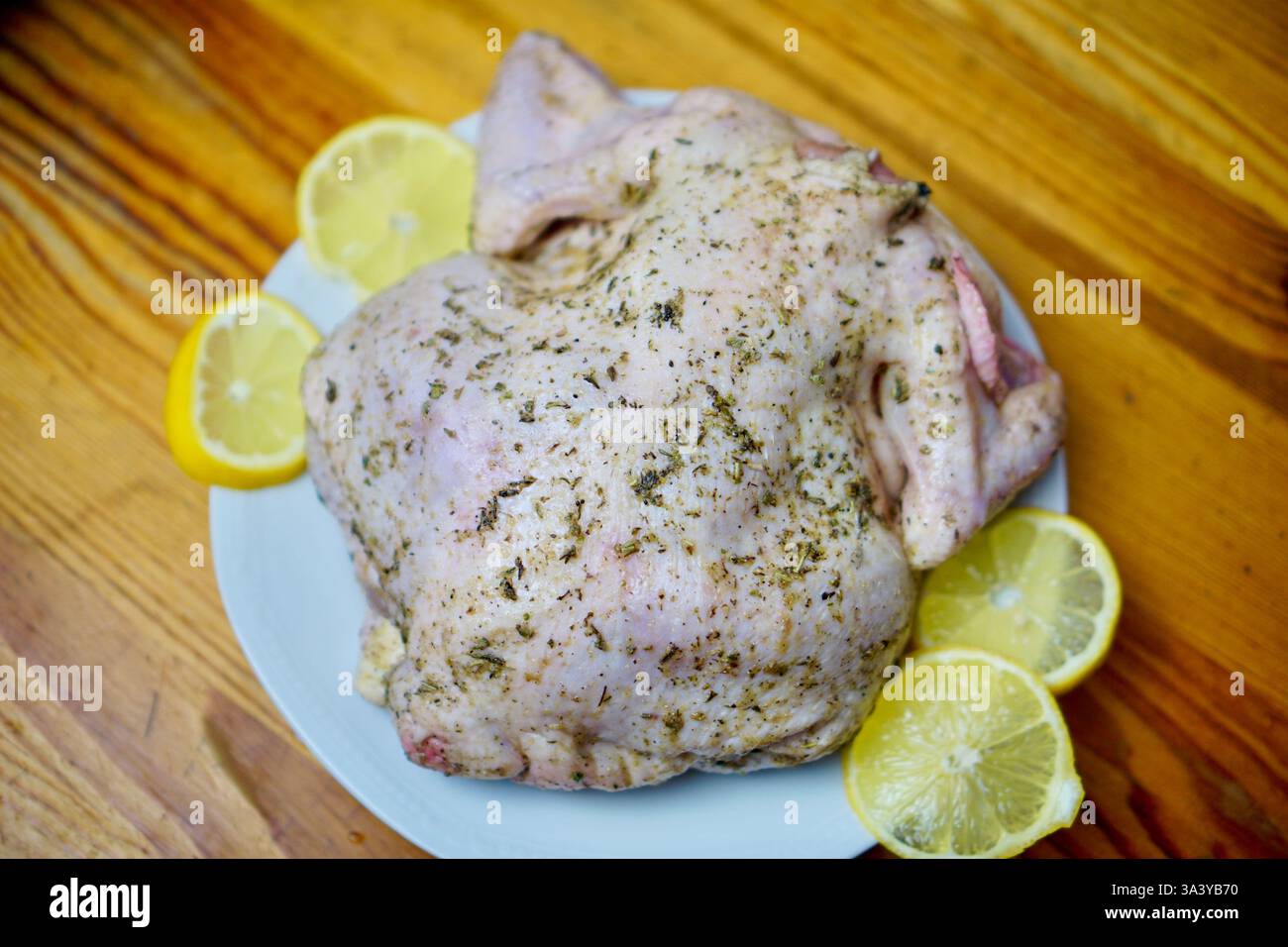 Poulet entier cru enrobé d'herbes aromatiques provençales et d'assaisonnements, placé sur une assiette blanche avec des tranches de citron frais sur une table en bois rustique. Le poulet est préparé pour la torréfaction, mettant l'accent sur la cuisine maison et la préparation des repas gastronomiques. Banque D'Images Poulet entier cru enrobé d'herbes aromatiques provençales et d'assaisonnements, placé sur une assiette blanche avec des tranches de citron frais sur une table en bois rustique. Le poulet est préparé pour la torréfaction, mettant l'accent sur la cuisine maison et la préparation des repas gastronomiques. Banque D'Images