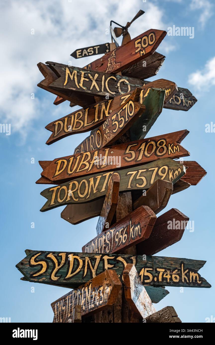 Signalisation sur un poteau en bois vers des destinations mondiales avec ciel bleu. Panneau indiquant les distances et les directions vers les pays et les villes de destination à partir du courant Banque D'Images