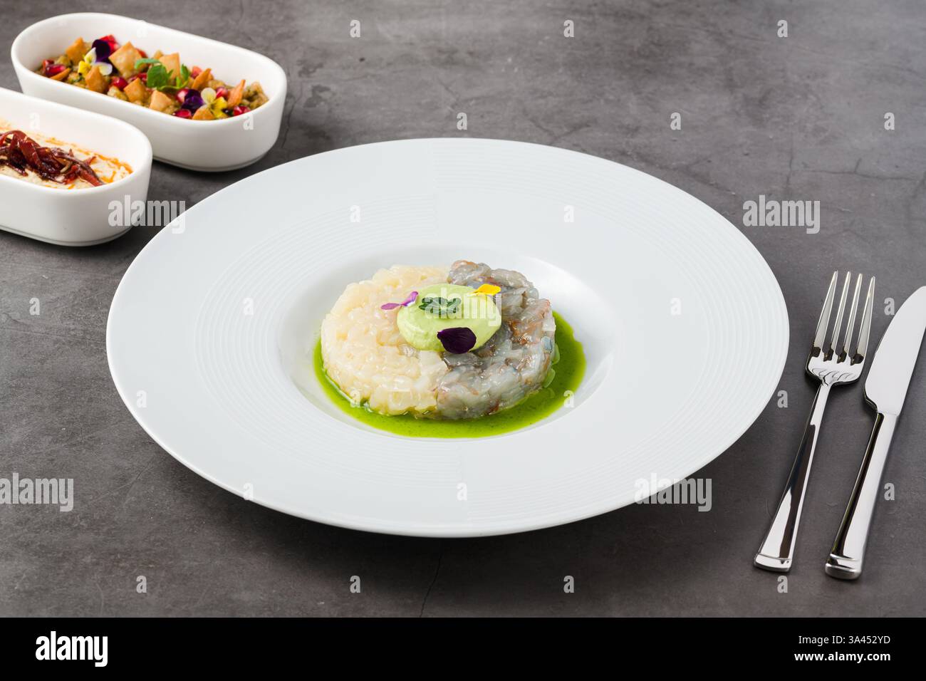 Tartare gourmand de crevettes et de poisson blanc avec mousse d'avocat, fleurs comestibles et sauce verte, servi dans une assiette blanche Banque D'Images