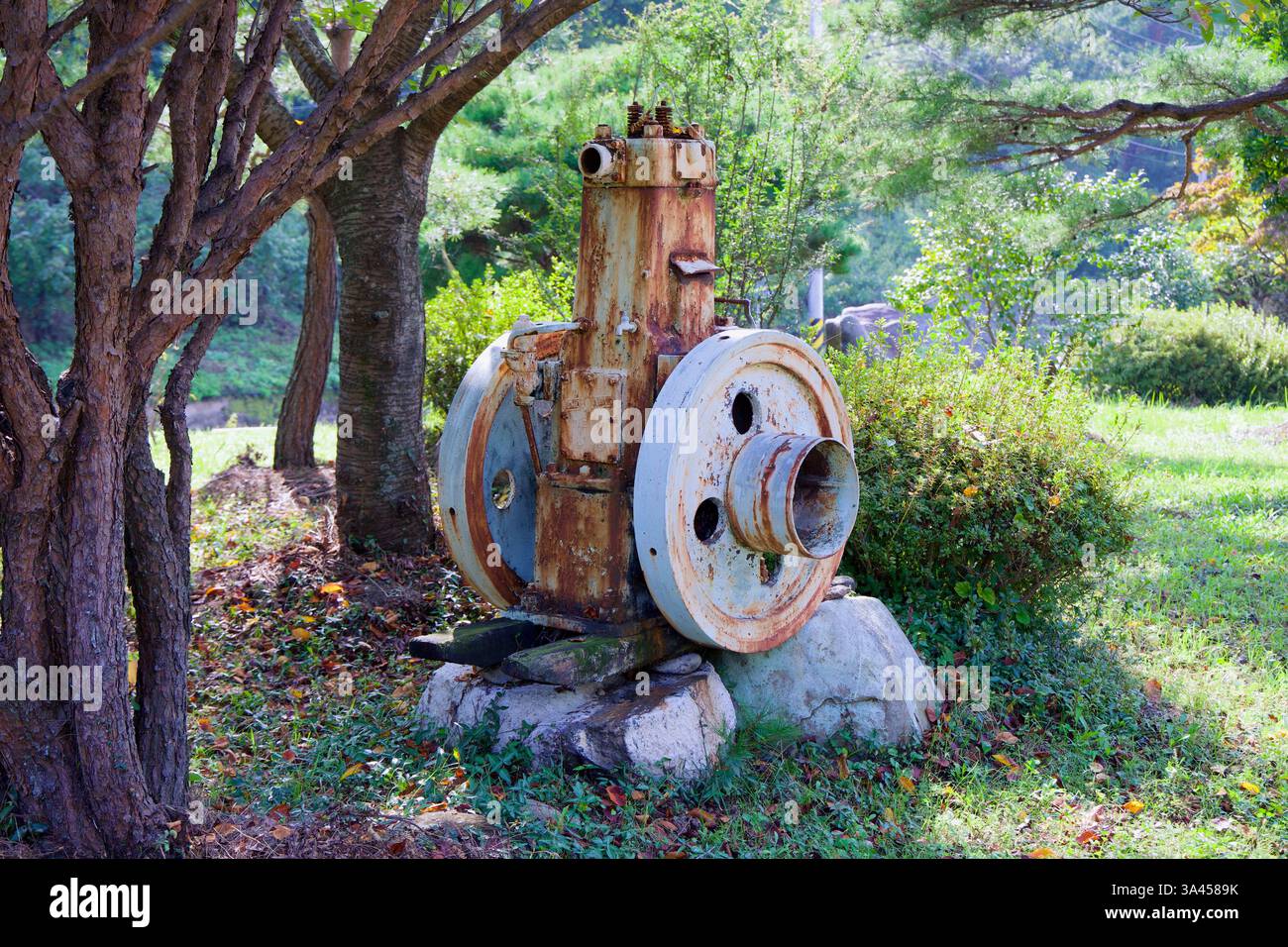 Gwangyang, Corée du Sud - 3 octobre 2021 : une machine industrielle abandonnée et rouillée se trouve sur une base de pierre sous l'ombre des arbres, se mélangeant Banque D'Images
