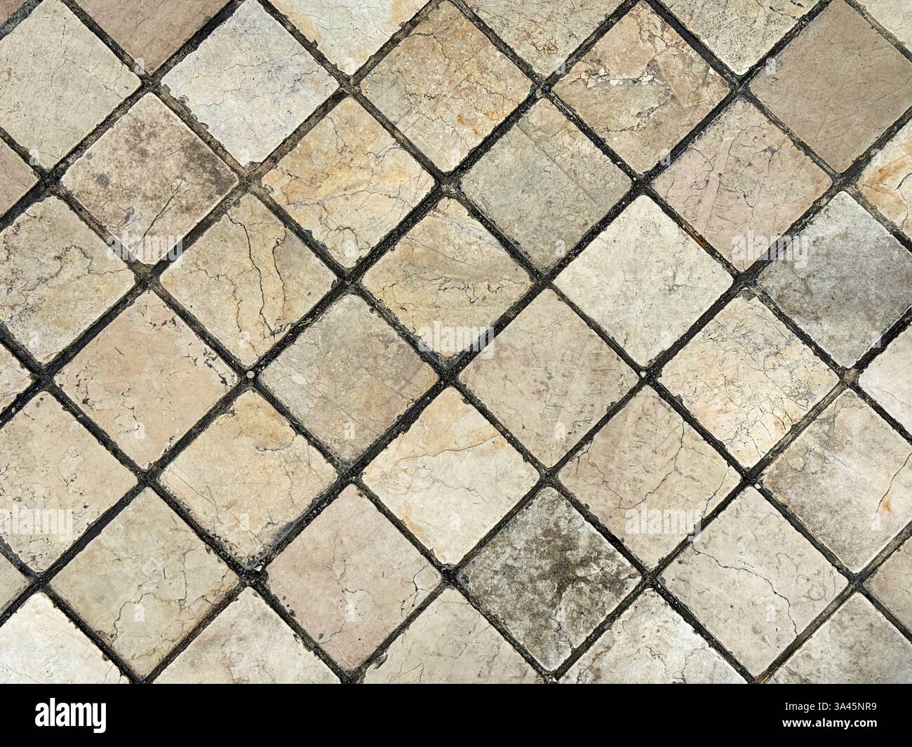 Carreaux de marbre en pierre naturelle en forme de diamant. Tuiles rodées extérieures avec des veines aléatoires de couleur jaune et beige avec des coulis noirs. mur ou sol Banque D'Images