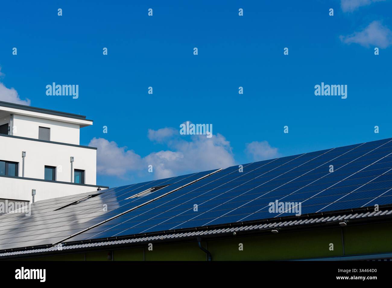 Des panneaux solaires sont installés sur le toit d’un bâtiment contemporain. Le ciel bleu vif est parsemé de quelques nuages moelleux, soulignant l'éco-ami Banque D'Images