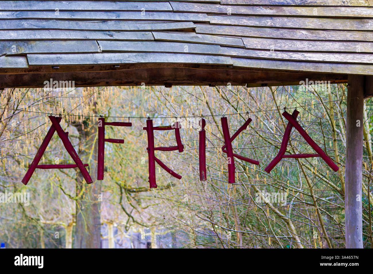 Rustique Afrika en bois signe dans la nature. Un panneau en bois avec le mot 'AFRIKA' en lettres rouges suspendu sous un toit rustique, entouré d'arbres. Banque D'Images