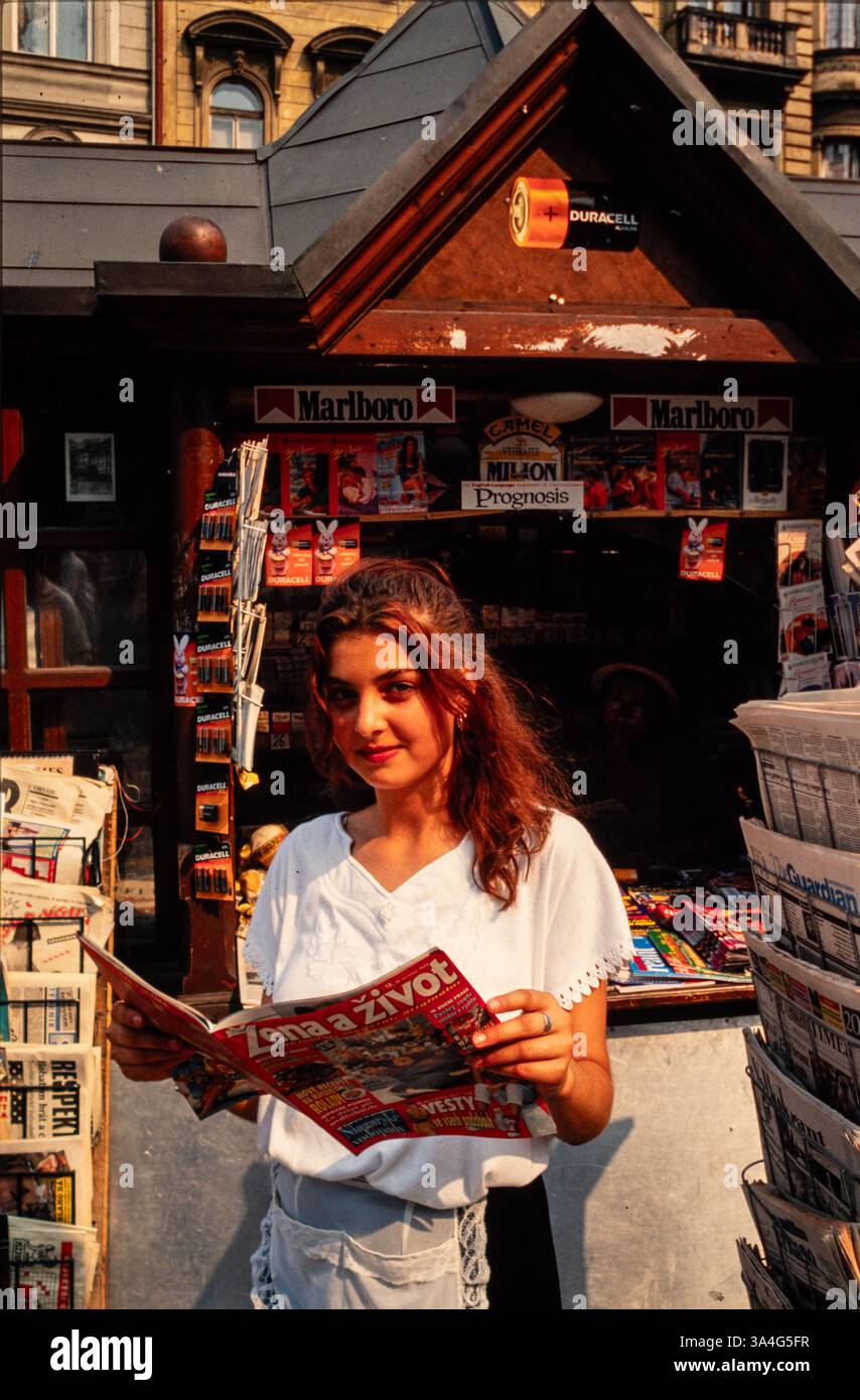 Une jeune femme travaillant dans un kiosque de rue à Prague, en Tchécoslovaquie, tenant un magazine. Le magasin vend également des cigarettes et des piles. Banque D'Images