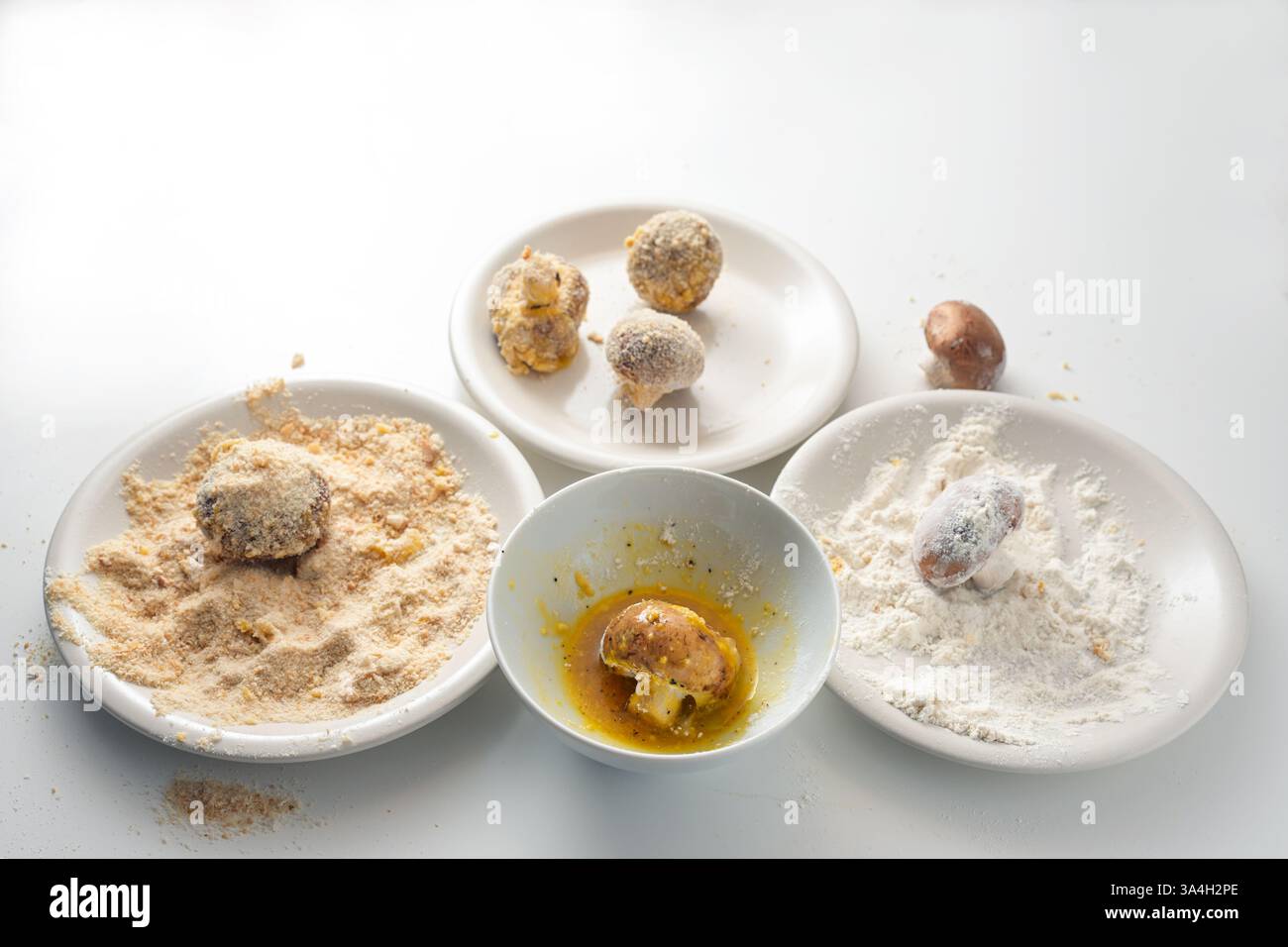 Les champignons crus sont panés dans des assiettes blanches avec de la farine, des œufs et de la chapelure pour être frits ou cuits au four, cuisiner des collations de fête à partir de légumes, Banque D'Images