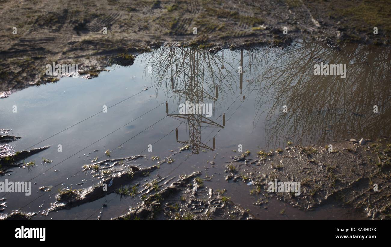 un gros plan regardant vers le bas une flaque boueuse avec un pylône reflété dans l'eau sale. Il est entouré de boue et a de l'espace pour copier le texte Banque D'Images