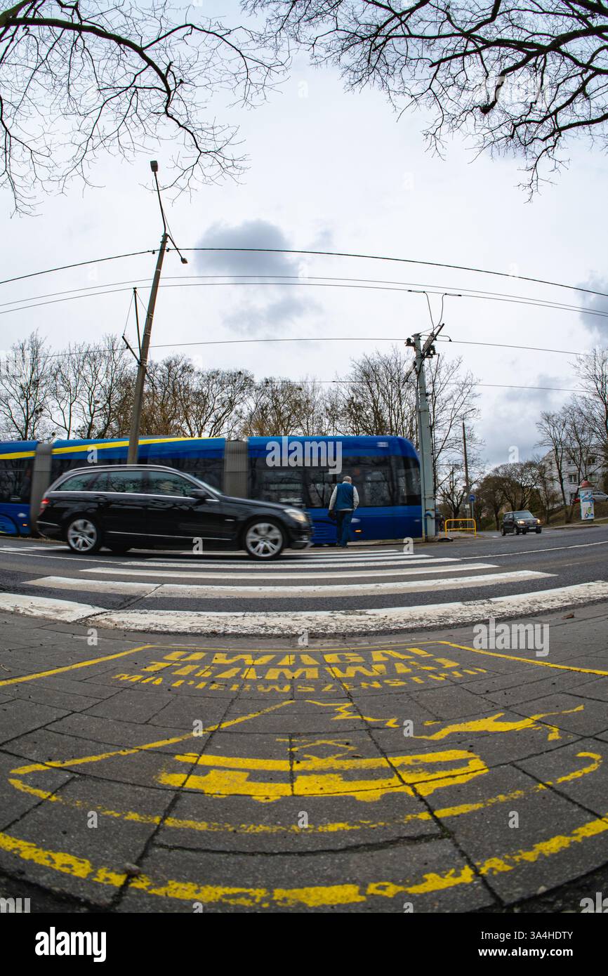 Un tramway bleu se déplace à travers l'intersection, rappelant aux piétons de regarder leur pas et d'attendre le transport prioritaire. Banque D'Images