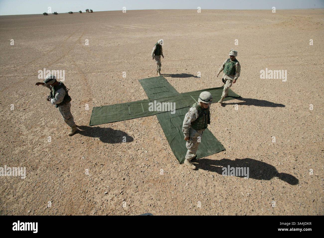 09 août 2004 ; Camp Korean Village, Irak ; alors qu’un chariot élévateur et d’autres véhicules de récupération attendent au loin, des Marines et des soldats étalent une toile X marquant une zone de largage pour les pilotes livrant des paquets de rations via un parachute près du Camp Korean Village, Irak, le 9 août 2004. De tels marqueurs au sol pourraient un jour être considérés comme obsolètes après le lancement du parachute cargo de précision Sherpa, un système produit commercialement et guidé par le système de positionnement global qui peut se diriger de près de cinq miles de haut à moins de 200 mètres d'un point de largage ciblé. Deux systèmes Sherpa ont fait leurs premiers débarquements dans un c. Banque D'Images