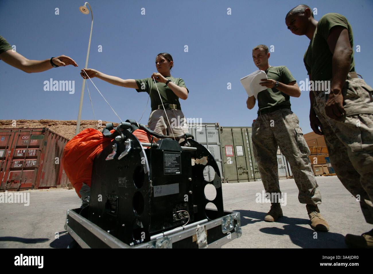 10 août 2004 ; Camp Al Asad, Irak ; le Cpl AMANDA J. RUSHAM, au centre, lance le Cpl DOUGLAS F. MILLER l'une des lignes de direction du système de parachutisme cargo de précision Sherpa, tandis que le Sgt BRIAN W. TRAFTON lit les instructions pour que les trois gréeurs de parachutistes de la 1re section de livraison aérienne puissent effectuer une vérification de fonctionnement de la machine au Camp Al Asad, Irak, le 10 août 2004. Le Sherpa est un système produit commercialement guidé par le système de positionnement global qui peut se diriger de près de cinq miles de haut à moins de 200 mètres d'un point de chute ciblé. Deux systèmes Sherpa ont fait leur d Banque D'Images