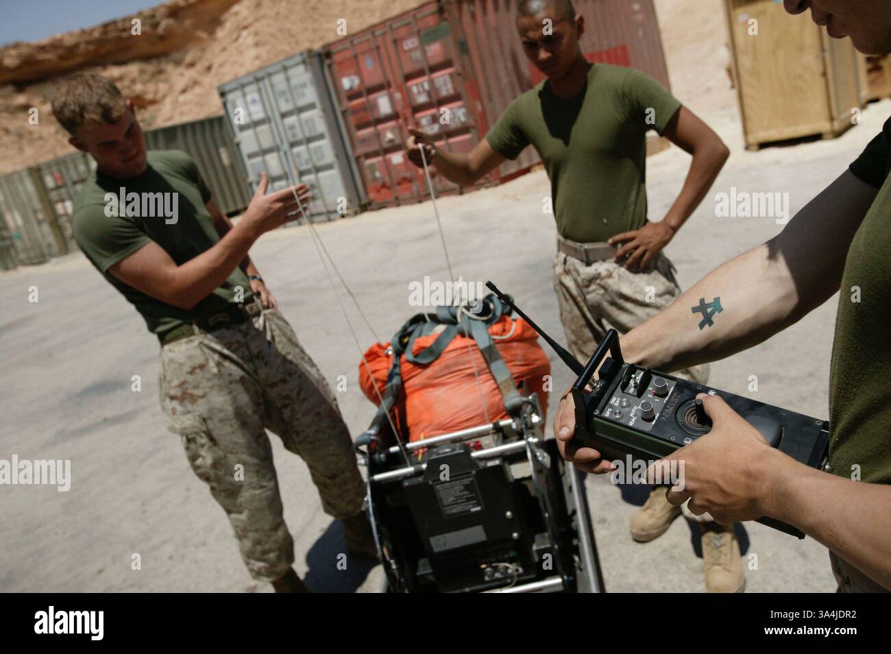 10 août 2004 ; Camp Al Asad, Irak ; le Cpl CHRISTOPHER J. HYMEL, utilise une télécommande pour tester les deux lignes de direction du système de parachute cargo de précision Sherpa, détenu par le Cpl DOUGLAS F. MILLER, à gauche, et le Cpl PEDRO PEREZ, afin que les trois gréeurs de parachutistes marins du 1er peloton de livraison aérienne puissent effectuer une vérification de fonctionnement de la machine au Camp Al Asad, en Irak, le 10 août 2004. Le Sherpa est un système produit commercialement guidé par le système de positionnement global qui peut se diriger de près de cinq miles de haut à moins de 200 mètres d'un point de chute ciblé. Deux systèmes Sherpa ma Banque D'Images