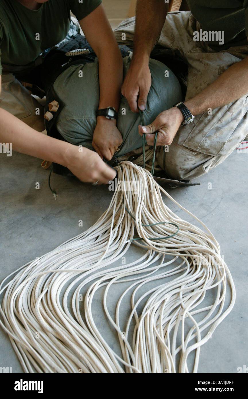 Le 10 août 2004 ; Camp Al Asad, Irak ; les gréreurs de parachute de la Marine du 1er peloton de livraison aérienne, le Cpl AMANDA J. RUHSAM, à gauche, et le Sgt BRIAN W. TRAFTON, remballent la canopée d'un système de parachute cargo de précision Sherpa au Camp Al Asad, Irak, le 10 août 2004, afin de la préparer pour sa prochaine mission. Deux systèmes Sherpa ont fait leurs débuts dans la zone de combat et des atterrissages de précision près du Camp Korean Village le 9 août. Le Sherpa est un système produit commercialement guidé par le système de positionnement global qui peut se diriger de près de cinq miles de haut à moins de 200 mètres d'un point de chute ciblé. Le pla Banque D'Images