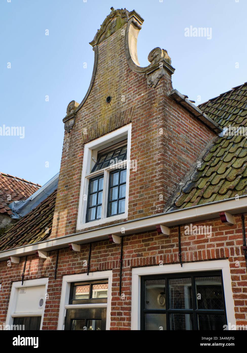 10 mars 2025 - Grou-pays-Bas : maison historique en brique néerlandaise avec une façade à pignon en gradins, fenêtres traditionnelles et tuiles de toit altérées sous un clair Banque D'Images