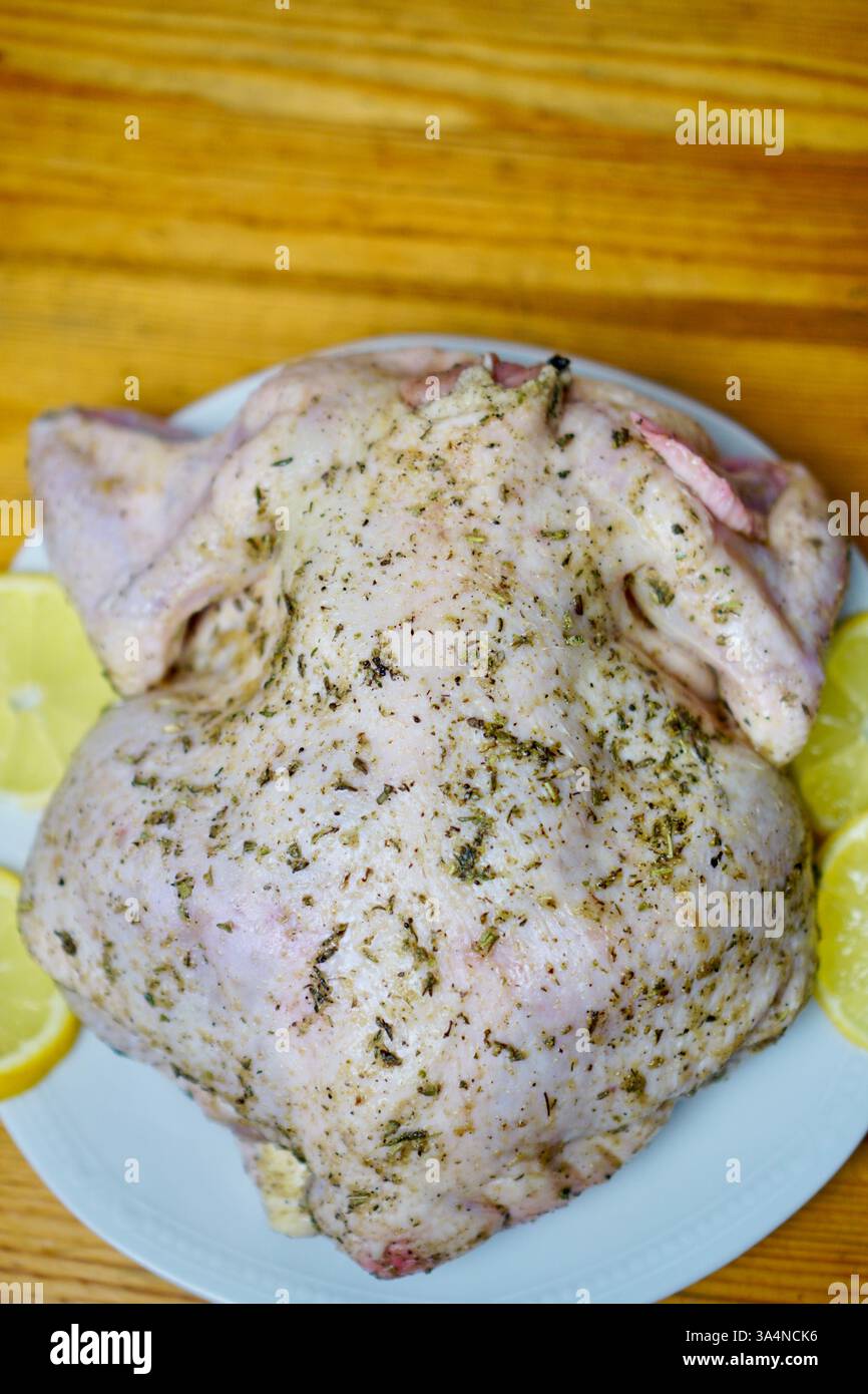 Poulet entier cru enrobé d'herbes aromatiques provençales et d'assaisonnements, placé sur une assiette blanche avec des tranches de citron frais sur une table en bois rustique. Le poulet est préparé pour la torréfaction, mettant l'accent sur la cuisine maison et la préparation des repas gastronomiques. Banque D'Images Poulet entier cru enrobé d'herbes aromatiques provençales et d'assaisonnements, placé sur une assiette blanche avec des tranches de citron frais sur une table en bois rustique. Le poulet est préparé pour la torréfaction, mettant l'accent sur la cuisine maison et la préparation des repas gastronomiques. Banque D'Images